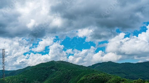 タイムラプス　夏の青空に流れるたくさんの白い雲と、新緑の山並み