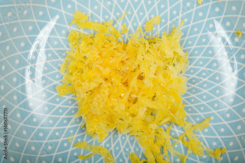 A close-up, top-down shot shows a pile of bright yellow lemon zest on a light blue decorative plate