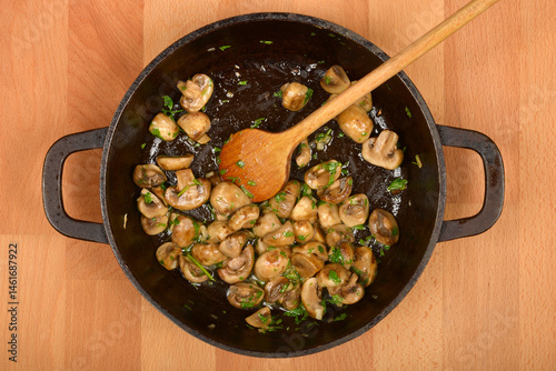Sauteed mushrooms with herbs are shown in a black cast iron skillet with a wooden spoon on a wooden surface