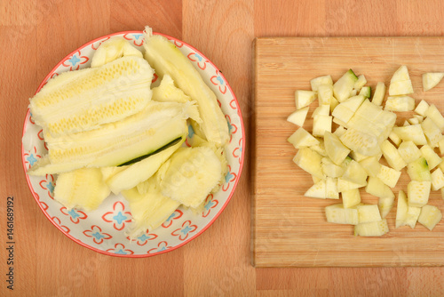 Peeled and chopped zucchini pieces are arranged on a patterned plate and a wooden cutting board, ready for cooking