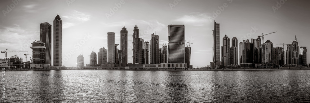 Fototapeta premium Monochrome city skyline with tall skyscrapers reflecting on calm water under a cloudy sky, Dubai Marina bay UAE