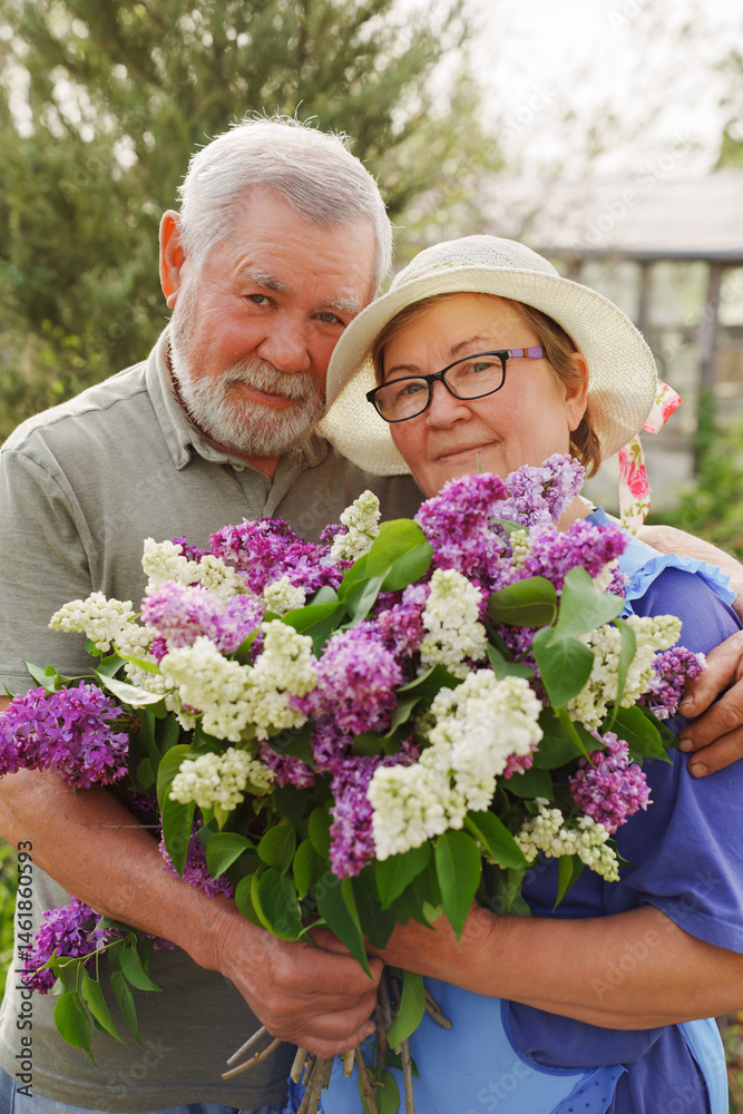 Older couple happily posing with a large bouquet of lilacs in a garden