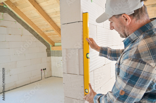 A construction worker carefully uses a level tool to ensure the wall is perfectly vertical, highlighting precision and craftsmanship in building projects