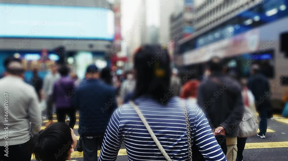 Crowded pedestrian crossing in Hong Kong, showcasing a diverse group of people navigating the busy street. Vivid urban environment with modern buildings in the background. Daytime atmosphere