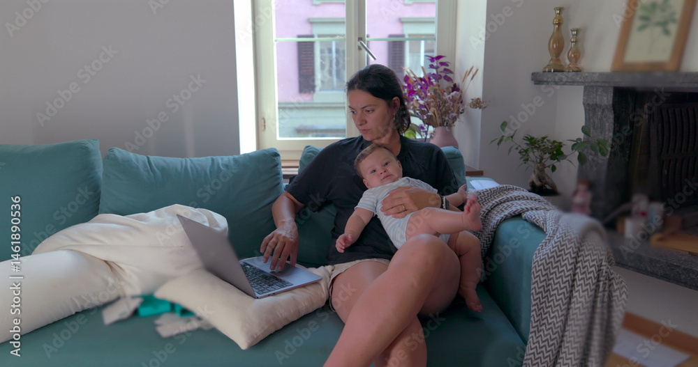 Obraz premium Mother holding baby on her lap while working on a laptop in a cozy living room, managing work and family time simultaneously, focused on her tasks