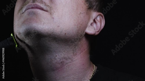 young man shaving his face with a trimmer for shaving his mustache and beard in a dark room 