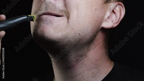 young man shaving his face with a trimmer for shaving his mustache and beard in a dark room 