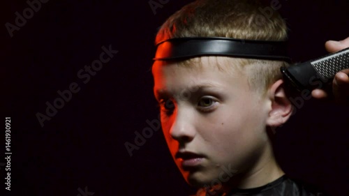 haircut of a young boy of the European region in a dark room in red light with a hair clipper