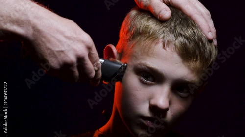 haircut of a young boy of the European region in a dark room in red light with a hair clipper