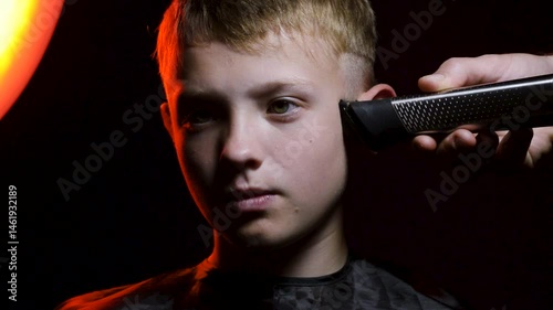haircut of a young boy of the European region in a dark room in red light with a hair clipper