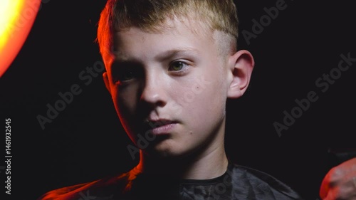 haircut of a young boy of the European region in a dark room in red light with a hair clipper