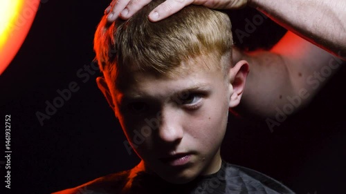 haircut of a young boy of the European region in a dark room in red light with a hair clipper