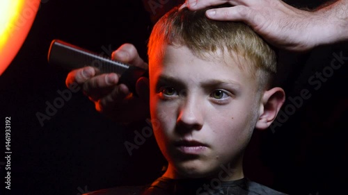 haircut of a young boy of the European region in a dark room in red light with a hair clipper
