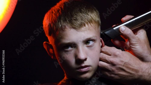 haircut of a young boy of the European region in a dark room in red light with a hair clipper