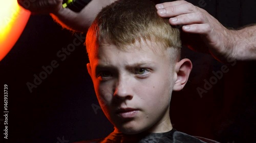haircut of a young boy of the European region in a dark room in red light with a hair clipper