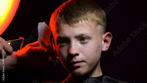 haircut of a young boy of the European region in a dark room in red light with a hair clipper