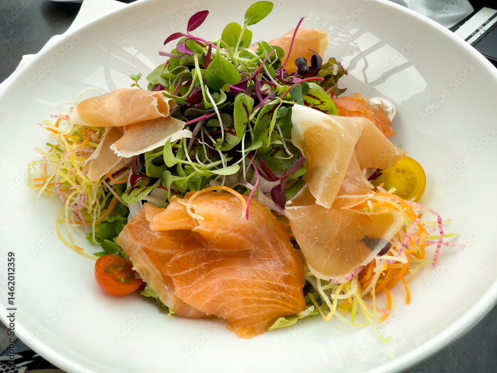 Fresh salad with thinly sliced beef and fish on white plate setting