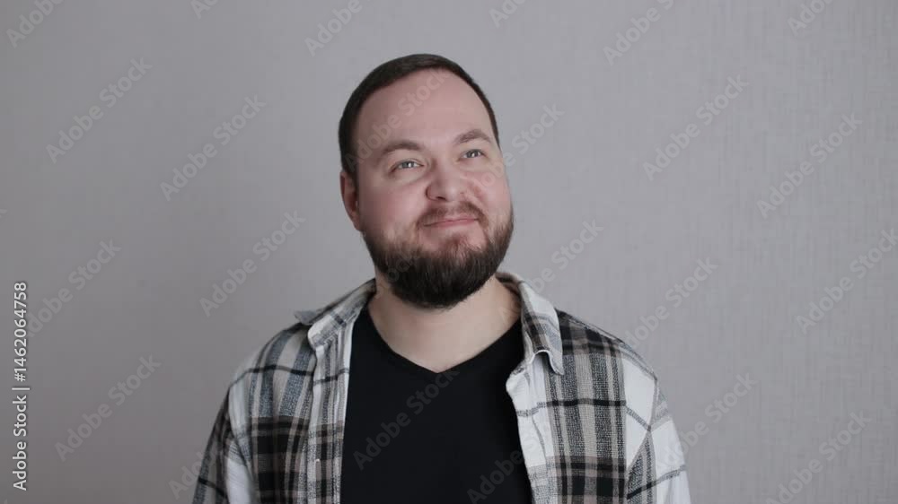 A bearded man is dreaming and smiling looking at the camera on gray background A bearded man is dreaming and smiling looking at the camera on gray background