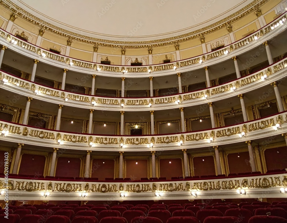 Obraz premium Elegant theater interior with ornate balconies, gold detailing, and plush red velvet seating.