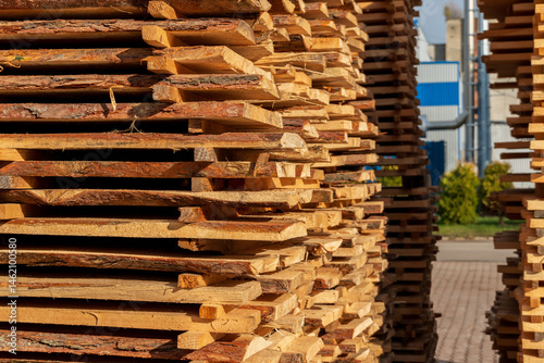Photos Piles of cut lumber arranged neatly at a sawmill, with sunlight highlighting the