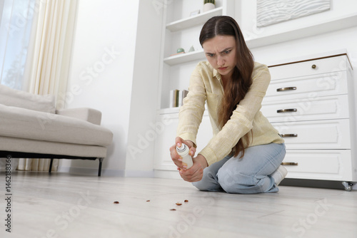 Emotional young woman spraying insecticide onto cockroaches on floor at home, space for text. Pest problem