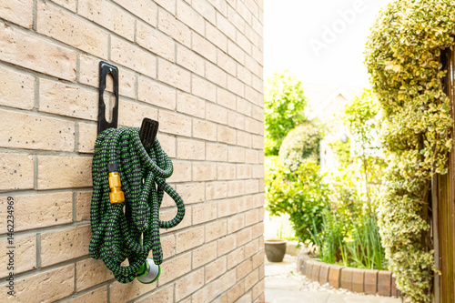 Shallow focus of a modern, self expanding garden hose seen hanging on its supplied hook on the outside of a private house brick wall. Part of the rear garden can be seen. photo