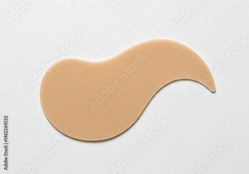 A tan colored silicone patch with a curved shape isolated on a white surface in a studio shot