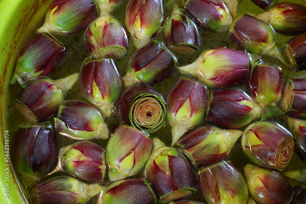 Many small fresh artichokes in brine in the stand of greengrocer