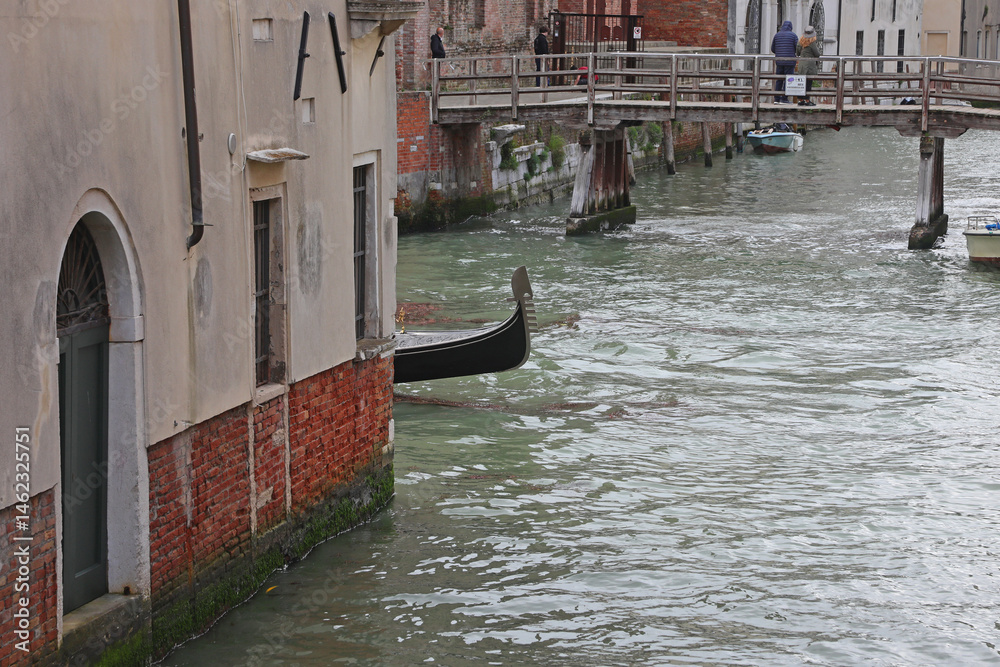 Bow of Gondola boat behind the corner of and houses on the navigagle waterway in Venice Island in Italy