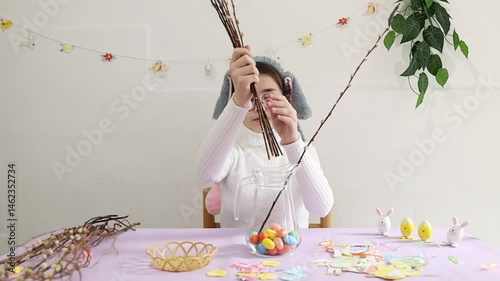 The girl puts willow branches into a glass jug.