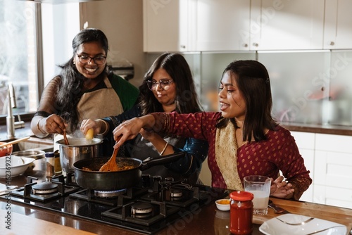 Foto Three adult South Asian women, wearing colorful ethnic clothing, cook a traditional meal together in a modern home kitchen, smiling and stirring food on the stove with fresh ingredients around them