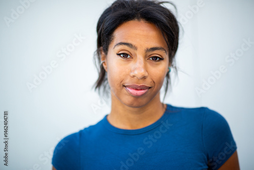 Close-up portrait of a young woman standing against a wight background, looking directly at the camera with a calm, confident expression