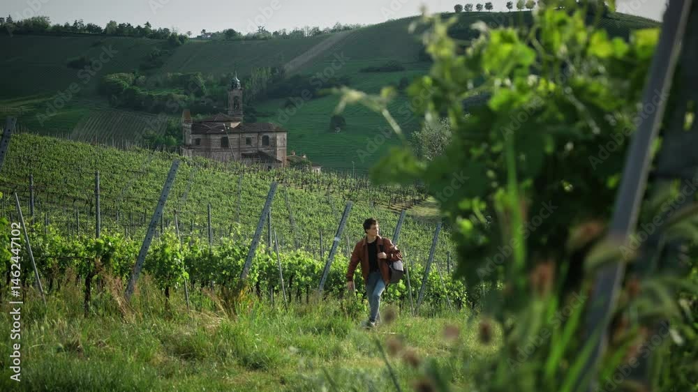 A young traveler in a leather jacket is hiking up a hill amid an incredible Italian landscape — an old Italian castle and sprawling vineyards. A young traveler in a leather jacket is hiking up a hill amid an incredible Italian landscape — an old Italian castle and sprawling vineyards.