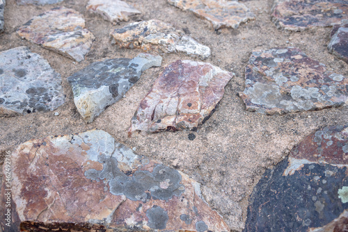 A close-up of weathered schist stones with natural lichen patterns, showcasing geological textures and rustic pavement construction, captured in Portugal