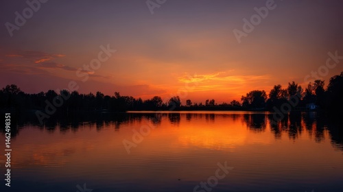 Vibrant sunset reflecting on calm lake water with silhouette of trees along the horizon line view