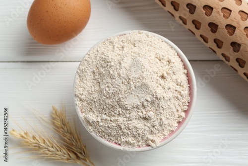 Flour in bowl, rolling pin, egg and spikes on white wooden table, flat lay