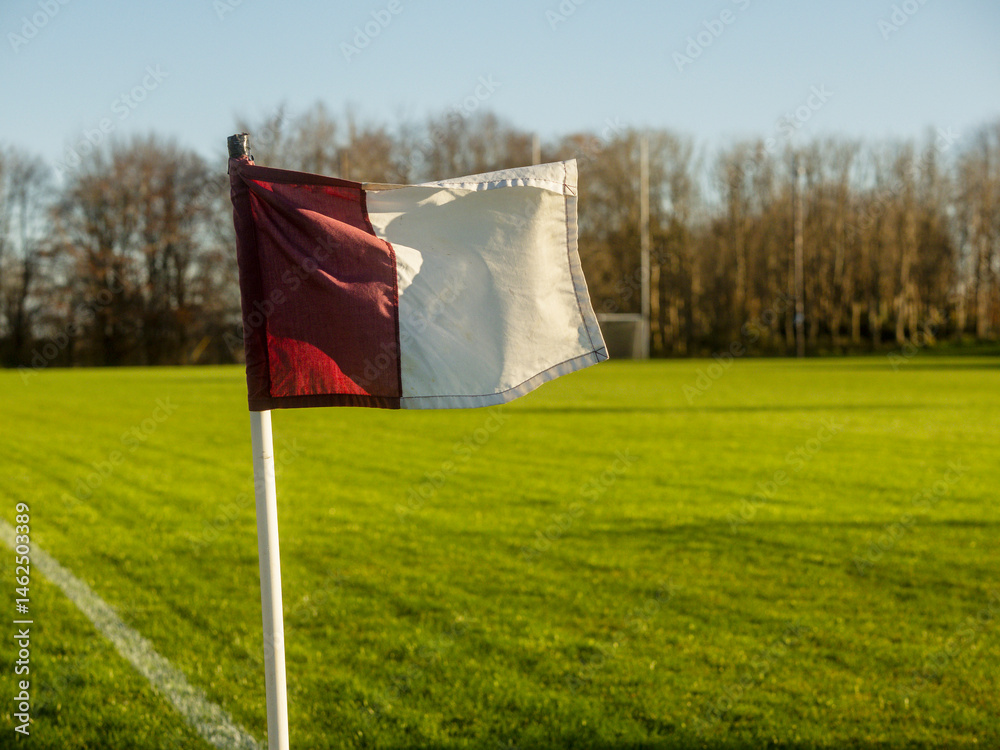 Maroon and white flag on a training pitch for camogie, rugby, hurling, Gaelic football. Irish sport ground in county Galway, Ireland. Warm sunny day. Tall goal posts in the background.