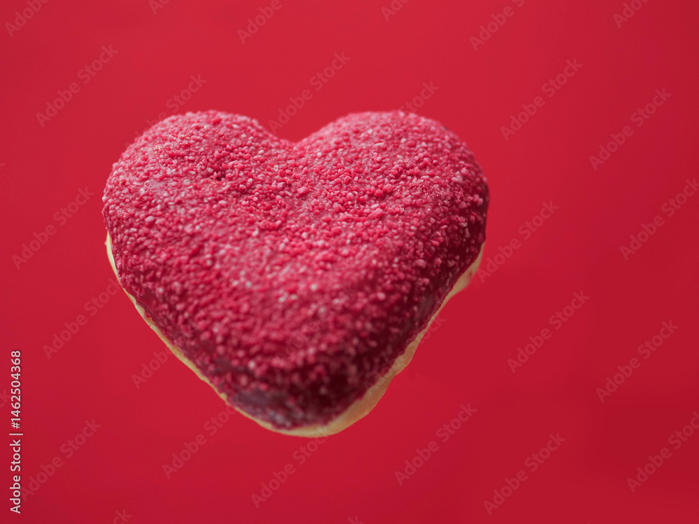 Red creative heart shaped donut floating in the air, red color saturated background. Love and romance concept. Valentine gift idea. Transforming food for marketing reasons to increase sales.