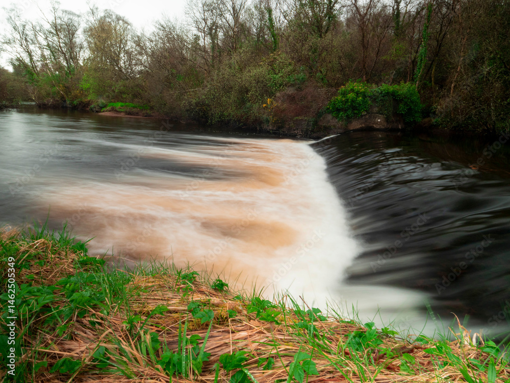 Small river with water flow. Trees and bushes growing on the river banks. Calm and relaxing nature scene.