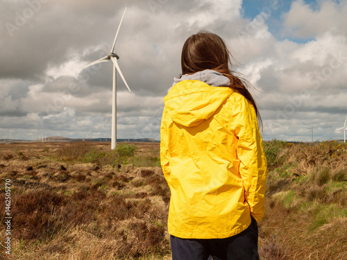 Obraz na płótnie Young teenager girl in yellow jacket, Wind turbines and vast wild fields in the background. Learning clean and green energy production. Warm sunny day. w salonie