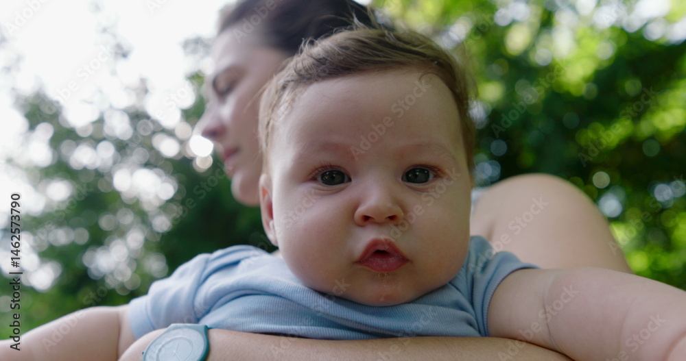 Close-up of a baby in mother’s arms, staring curiously with wide eyes, focus on facial expression and the close bond shared between them in an outdoor setting, greenery in background Close-up of a baby in mother’s arms, staring curiously with wide eyes, focus on facial expression and the close bond shared between them in an outdoor setting, greenery in background