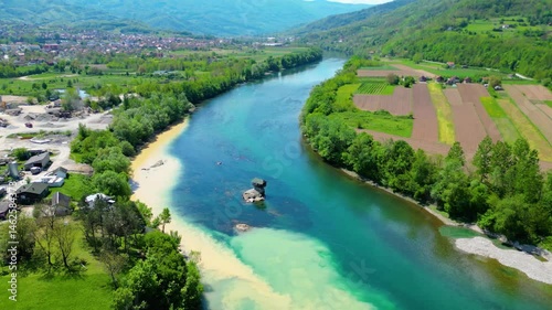 Aerial view of Bajina Bašta and the iconic Kućica na Drini (Drina River House), peacefully perched on a rock in the middle of the emerald Drina River, surrounded by lush nature and mountain landscapes