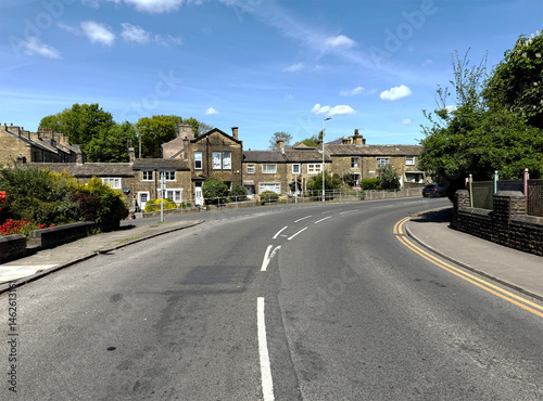 Fototapeta Naklejka Na Ścianę i Meble -  Leylands Lane, curves past old cottages in the small village of Heaton, The empty street suggests a quiet moment in the day, and the well-maintained gardens add charm to the scene.