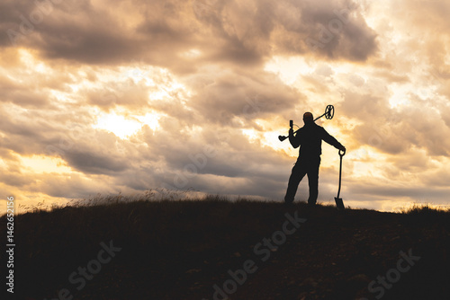 the silhouette of a man against the sunset, a metal detector slung over his shoulder