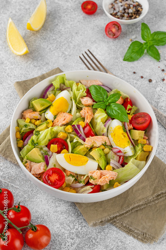 Salmon salad with avocado, boiled eggs, sweet corn, tomatoes, lettuce and red onion on concrete background. Healthy food. Top view.