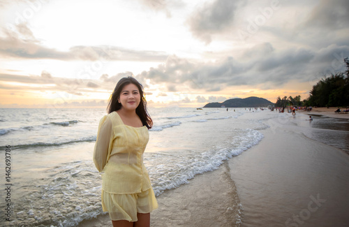 Beautiful Asian woman walking peacefully on a desert beach during sunset, with freedom concept, with amazing orange sky and sunlight reflecting on the sea and sand.