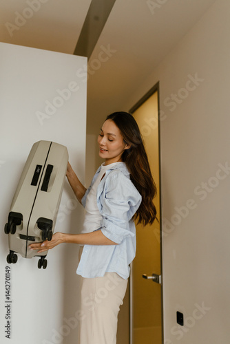 Obraz na płótnie A woman stands and smiles while holding a suitcase, in the corridor w salonie