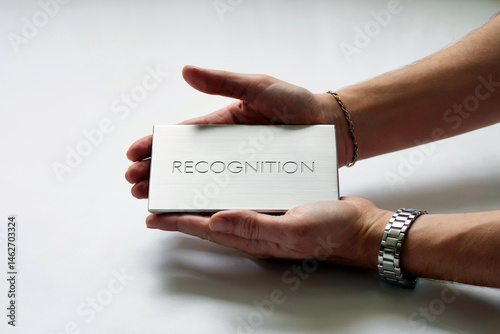 A pair of hands gently holds a sleek, metallic plaque engraved with the word 
