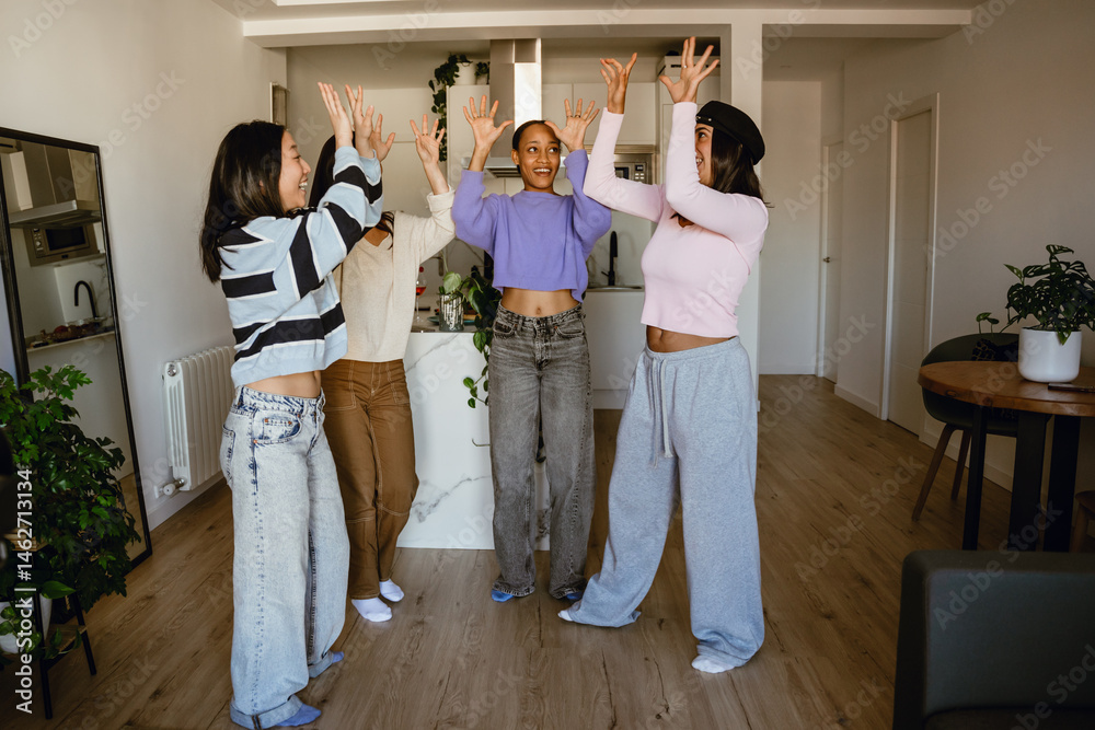 Group of four female friends standing with their hands raised and laughing