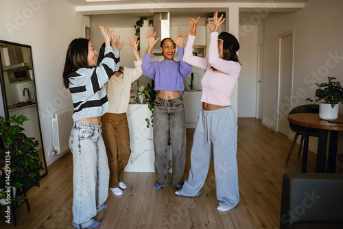 Obraz na płótnie Group of four female friends standing with their hands raised and laughing w salonie